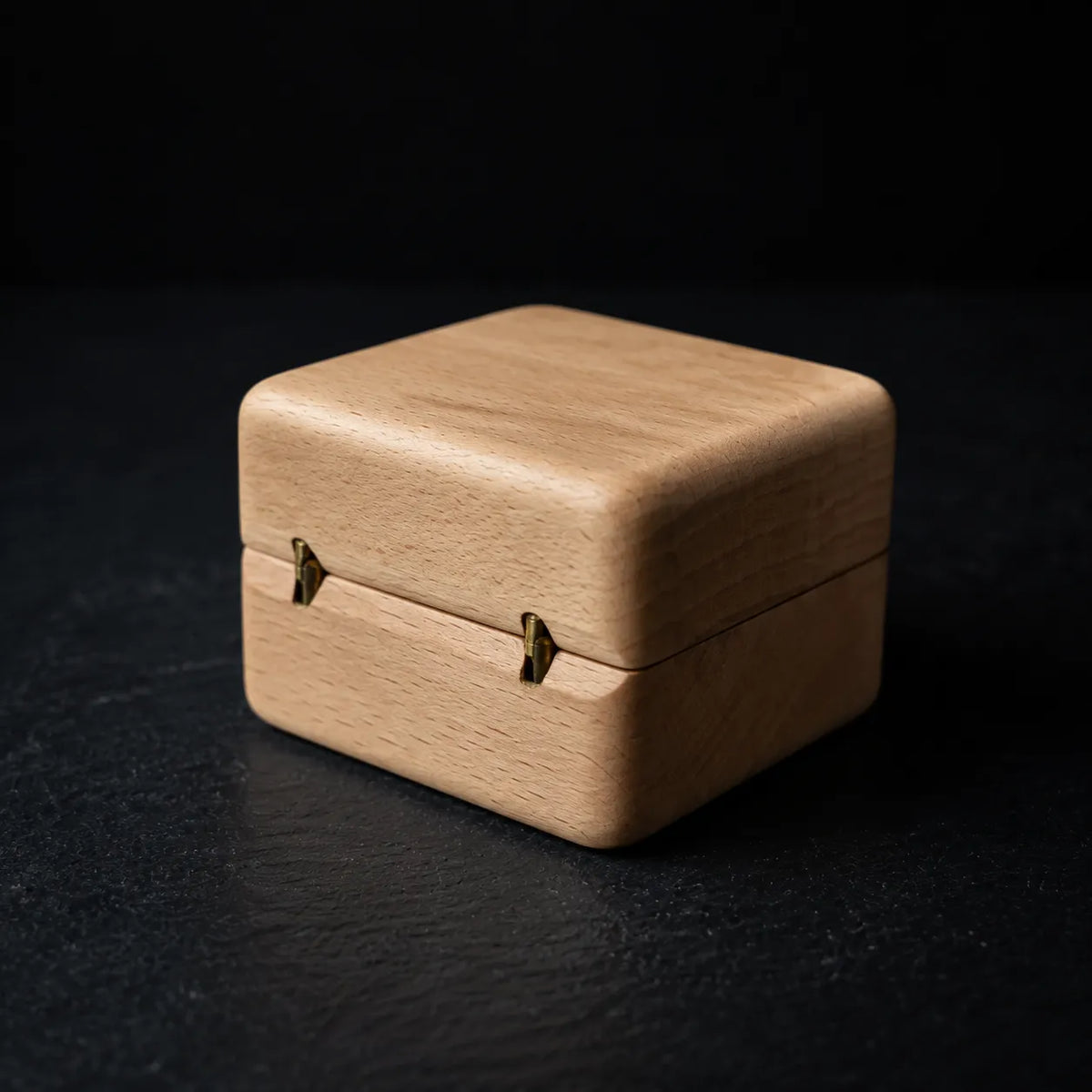 Closed natural wood ring box showing the rear brass hinges on a black background