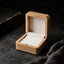 Open natural wood ring box with white velvet interior on a dark collector’s desk