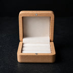 Open natural wood ring box with white velvet ring slots, shown from the front on a black background