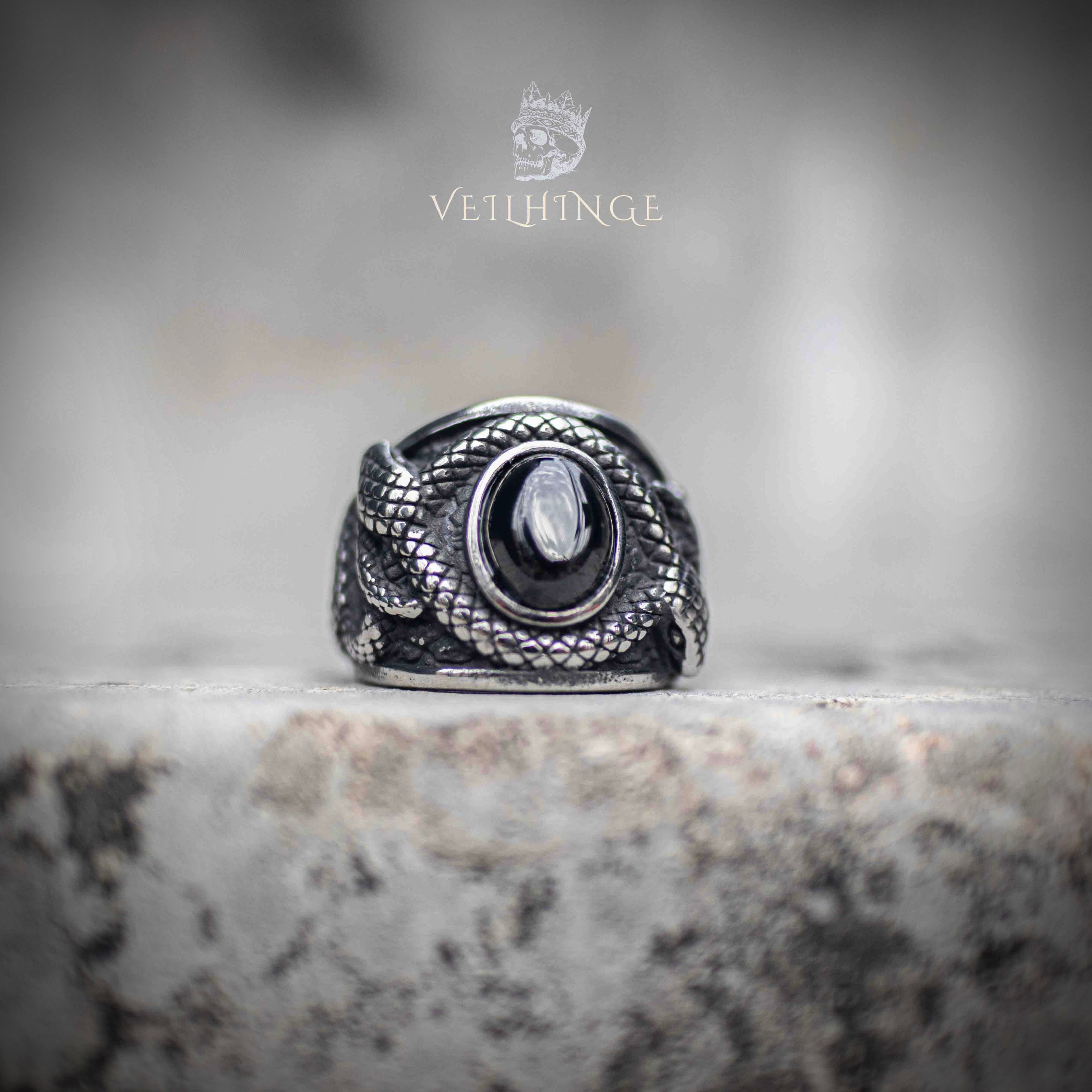 Coiled snake ring with oval obsidian stone centerpiece — silver serpent scales wrapping both sides, front view on stone surface