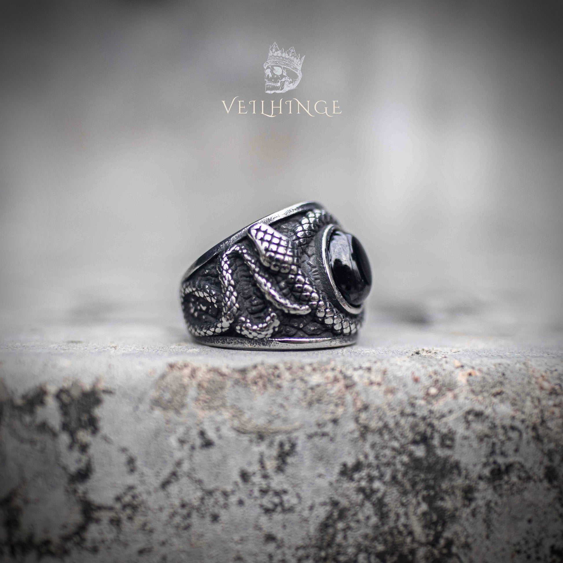 Side angle of coiled serpent ring showing textured snake scale engraving and obsidian cabochon set at center — oxidized silver finish