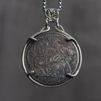 Viking Odin coin pendant set in a four-prong open bezel with ornate skull bail, obverse face forward on a box chain, dark stone background
