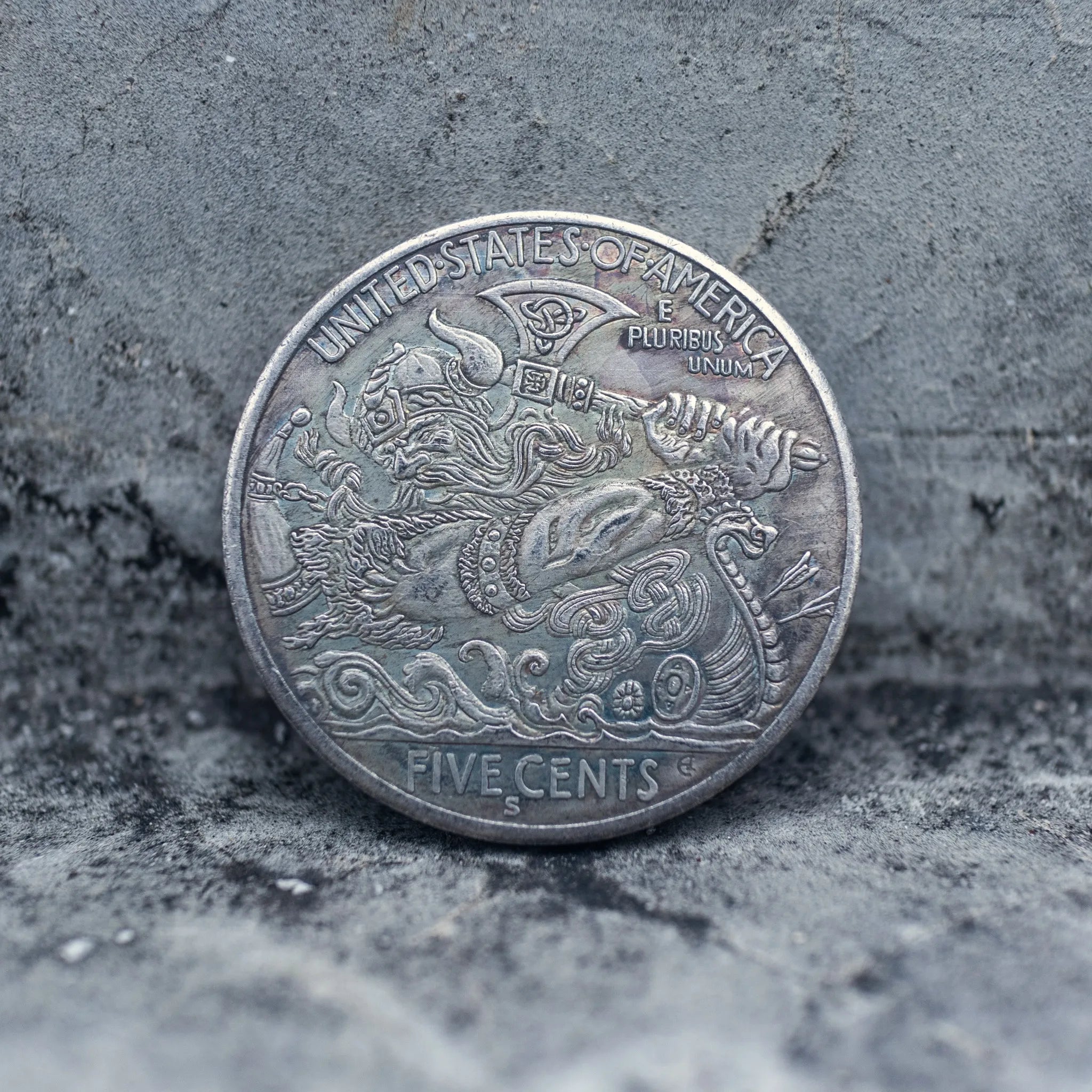 Hobo nickel coin engraved with Odin in a horned helmet wielding an axe aboard a dragon-prow Viking longship, Five Cents obverse face on stone background