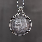 Book lover coin pendant reversed to the One More Chapter side showing a reader surrounded by stacked books and bookshelves, held in a four-prong bezel on a chain