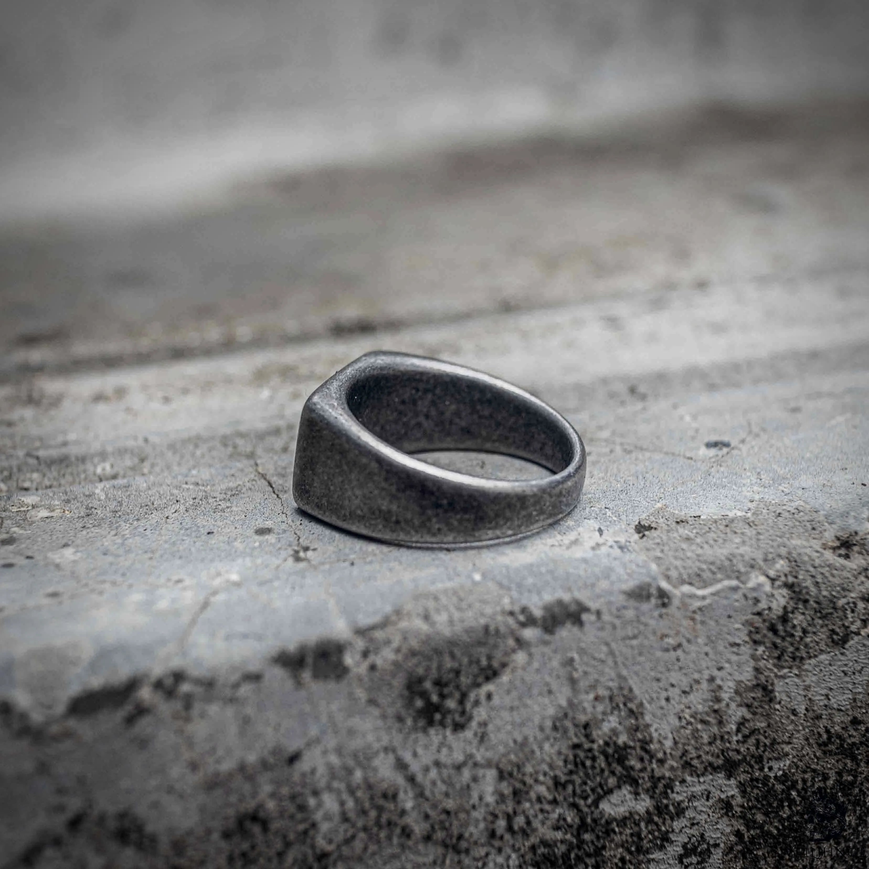 Oxidized black signet ring angled view showing blank rectangular face and rounded sandblasted stainless steel band, minimalist dark aesthetic ring by Veilhinge