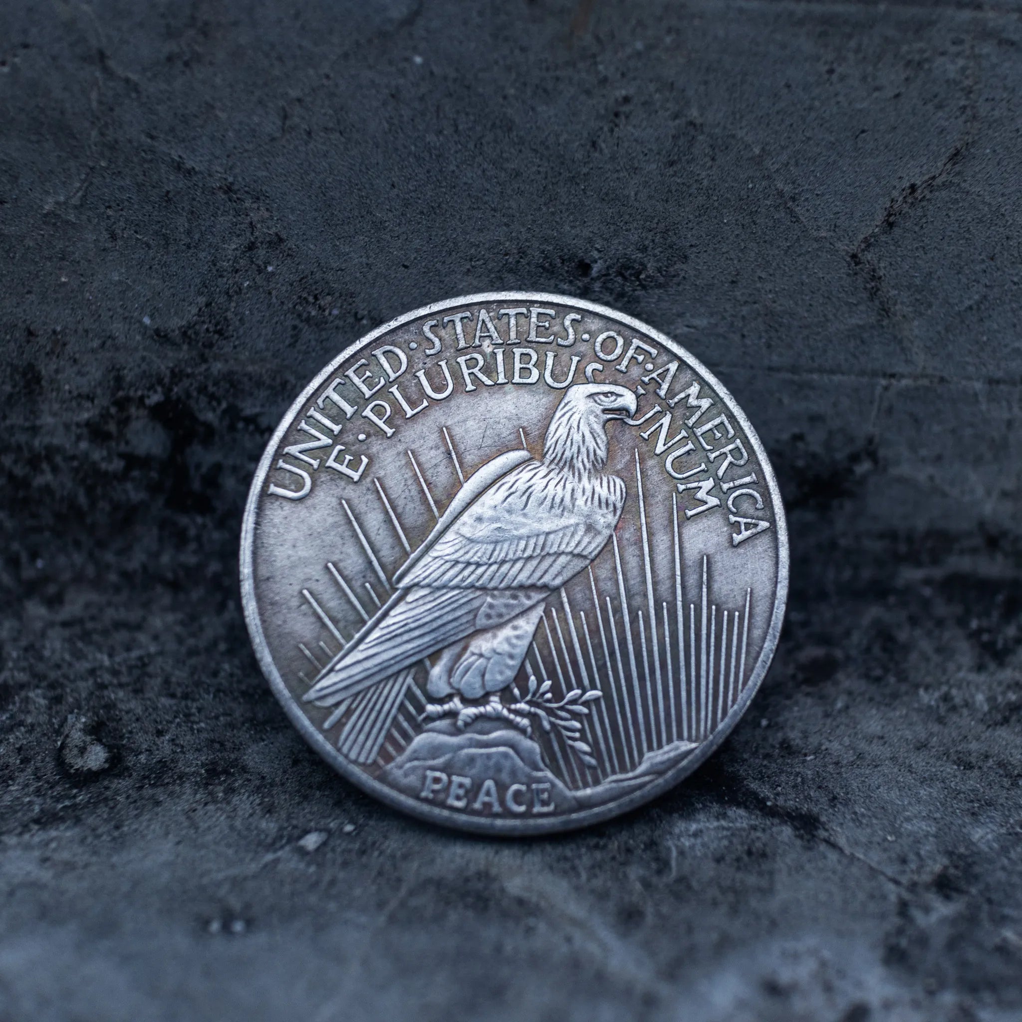 Peace Dollar reverse showing a standing eagle, E Pluribus Unum, United States of America, and Peace inscription at base on dark stone surface