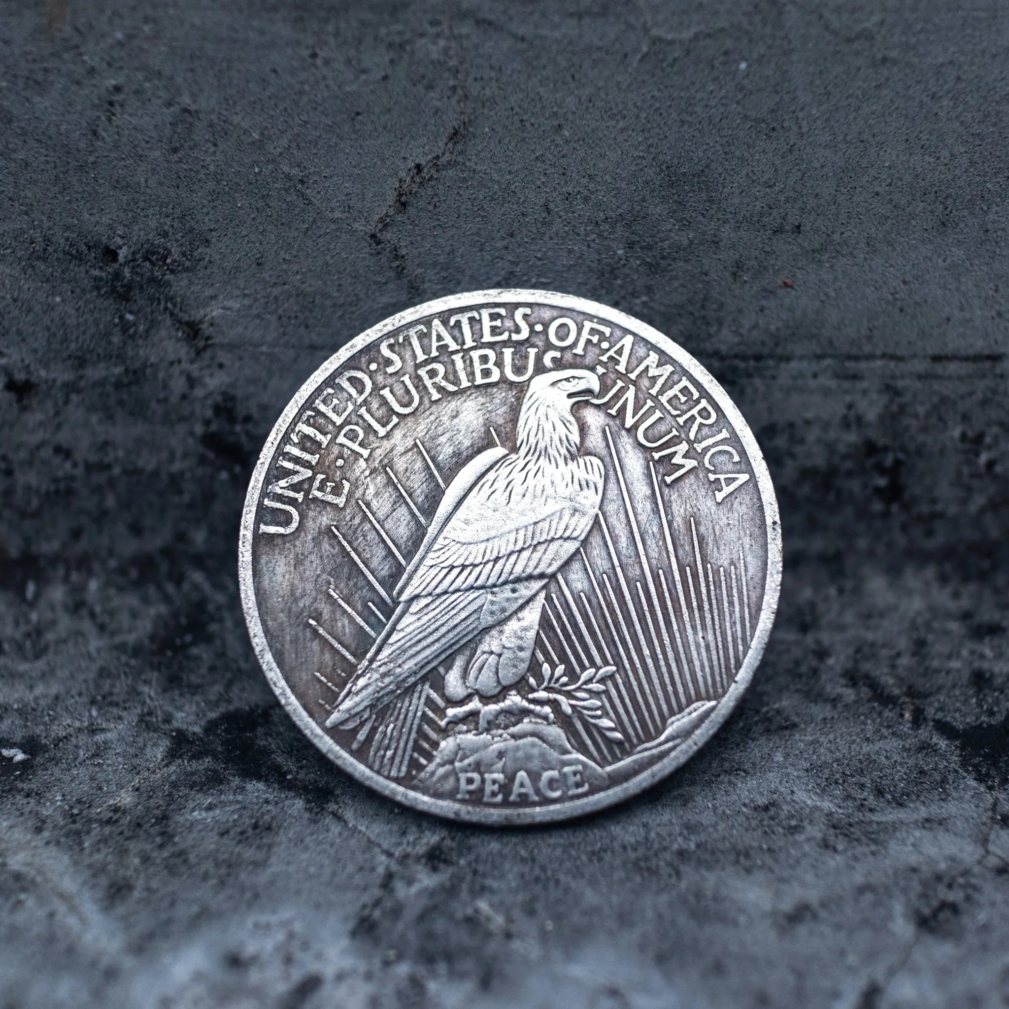 Peace Dollar reverse showing a standing eagle, E Pluribus Unum, United States of America, and Peace inscription at base on dark stone surface