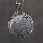 Coin pendant engraved with a bearded pirate captain skull face in tricorn hat with compass badge, ship wheel detail, set in a four-prong bezel on a box chain