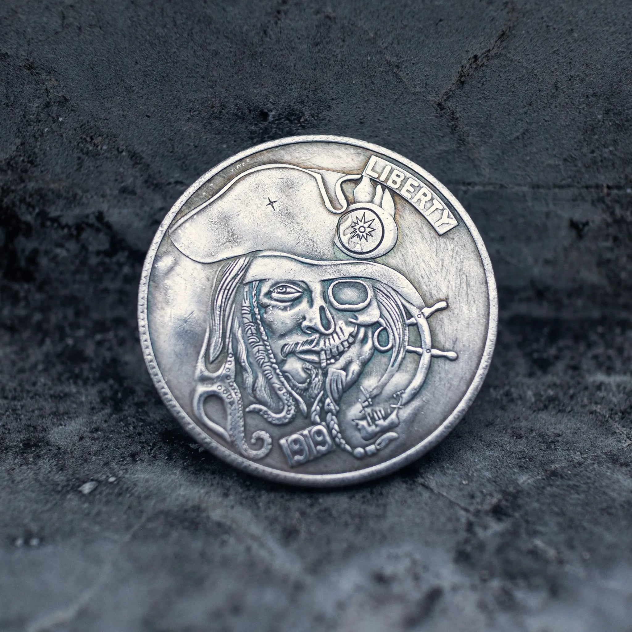 Close-up of a coin engraved with a bearded pirate captain skull in tricorn hat, compass badge on hat, Liberty inscription, dated 1913, ship wheel at lower right