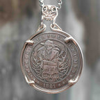 Coin pendant engraved with a plague doctor in a beak mask and long robe surrounded by skull and vine details, dated 1881, set in a four-prong bezel on a chain