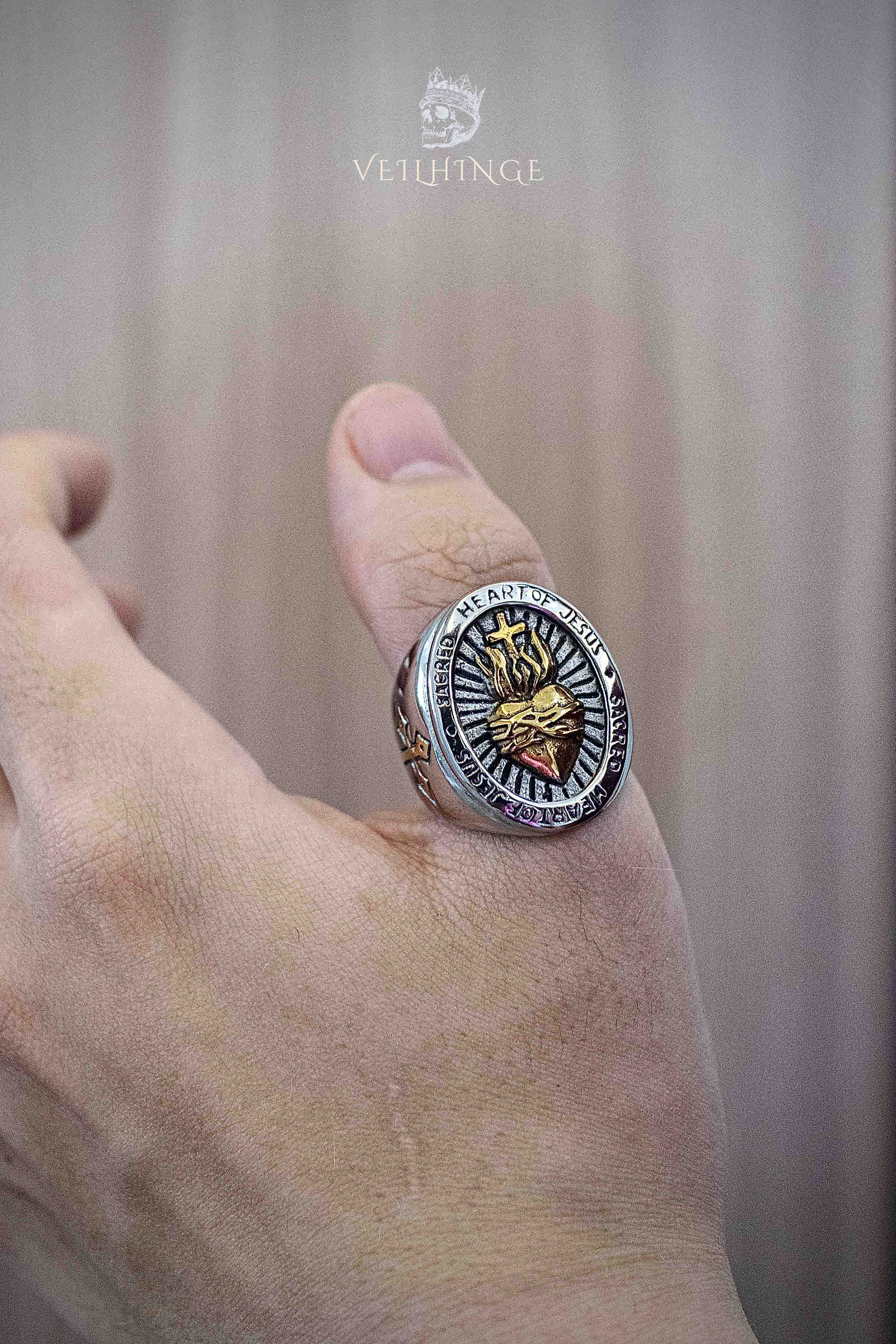 Sacred Heart of Jesus ring worn on the back of a hand — gold flame and crown of thorns motif on a silver oval face, two-tone religious signet ring