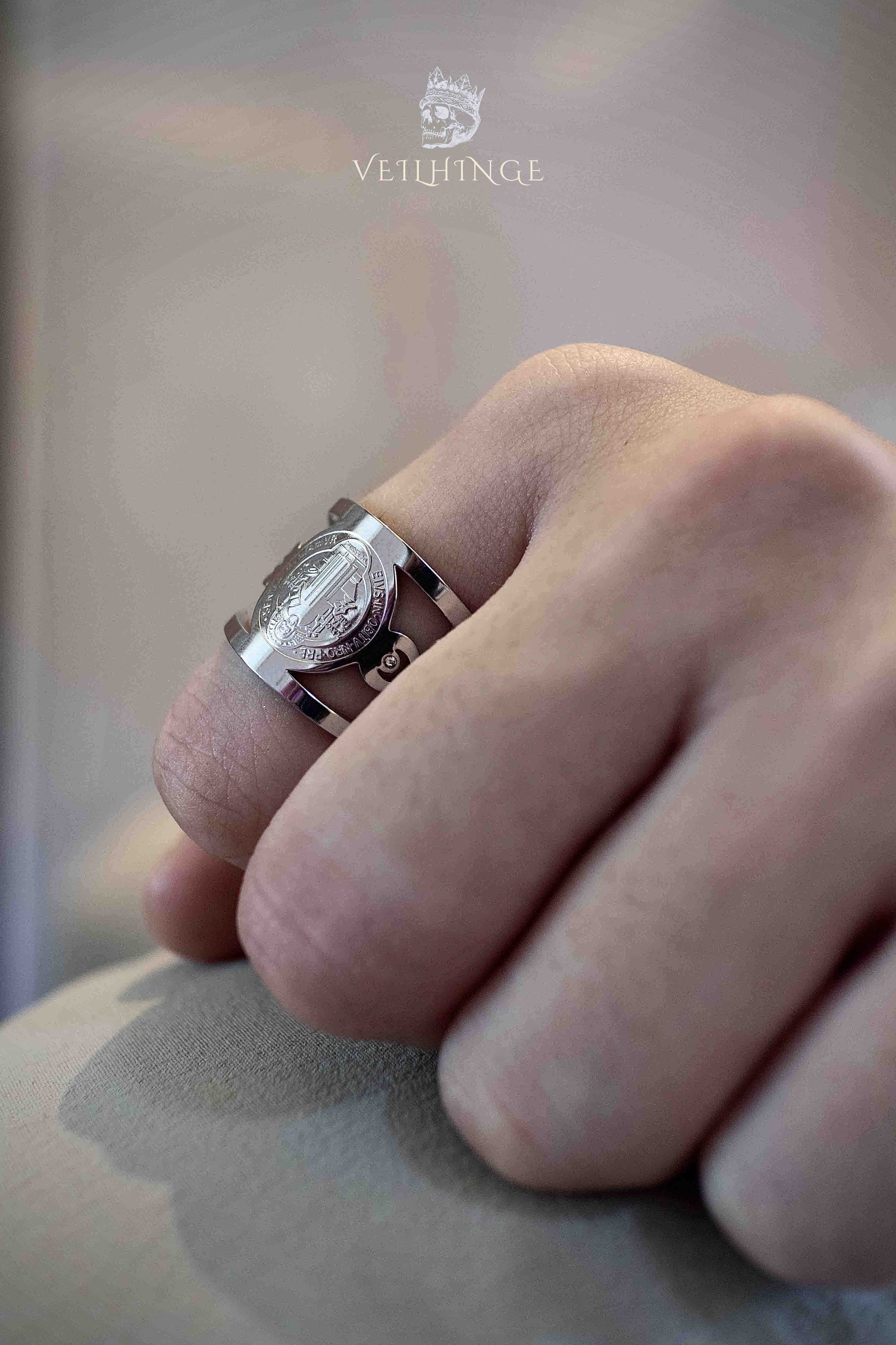 Saint Benedict ring viewed from above on a loosely clenched hand, polished silver cutout band with the medal centered on top