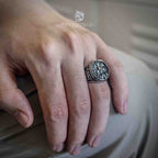 Saint George Dragon Slayer signet ring in oxidized silver worn on a relaxed hand, medieval battle scene engraved on the face with scrollwork shoulders