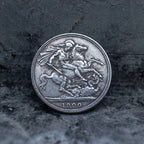 Close-up of a coin engraved with Saint George on a rearing horse driving a lance into a dragon below, dated 1900, on dark stone surface