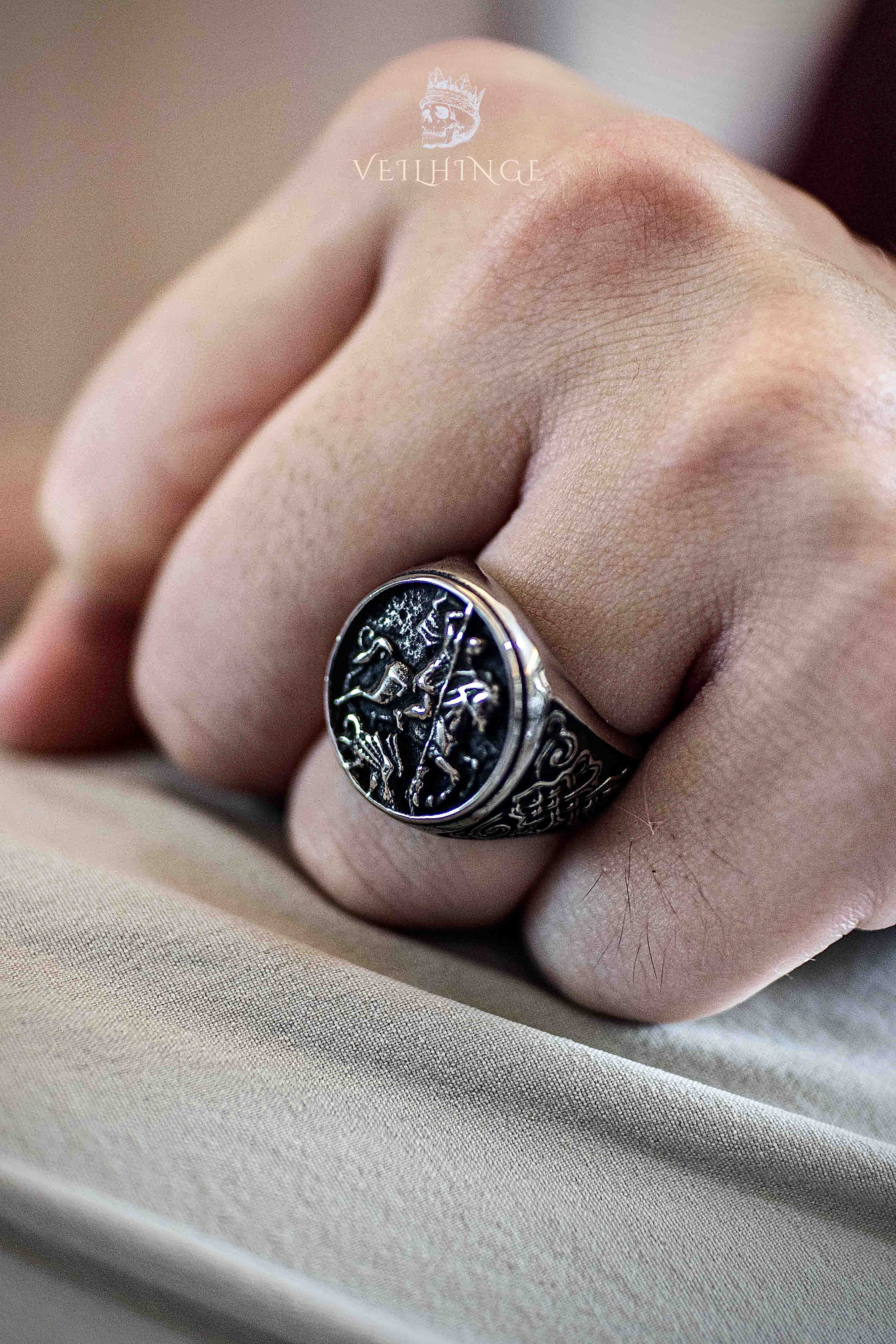 Saint George slaying the dragon engraved on an oxidized signet ring, worn on a clenched fist — medieval knight ring close-up