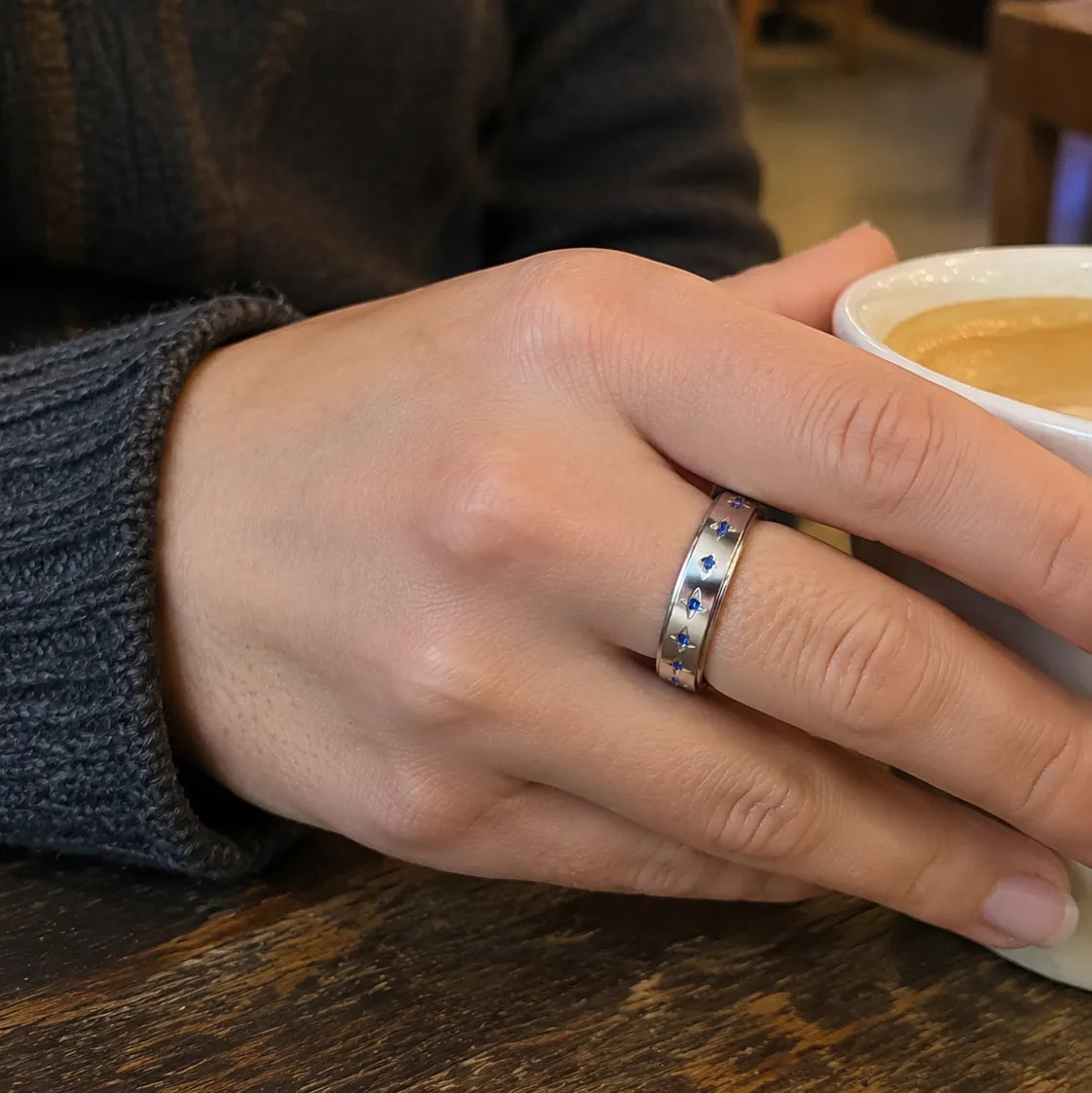 Woman wearing a polished silver spinner ring with staggered blue stones and engraved star details