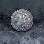 Close-up of a hobo nickel style coin engraved with a skeleton holding a fan of playing cards, flame and feather background, rope border, E Pluribus Unum, dated 1890