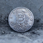 Close-up of a coin engraved with a skull in aviator goggles and flight jacket, Liberty and In God We Trust inscriptions, dated 1942, on dark stone