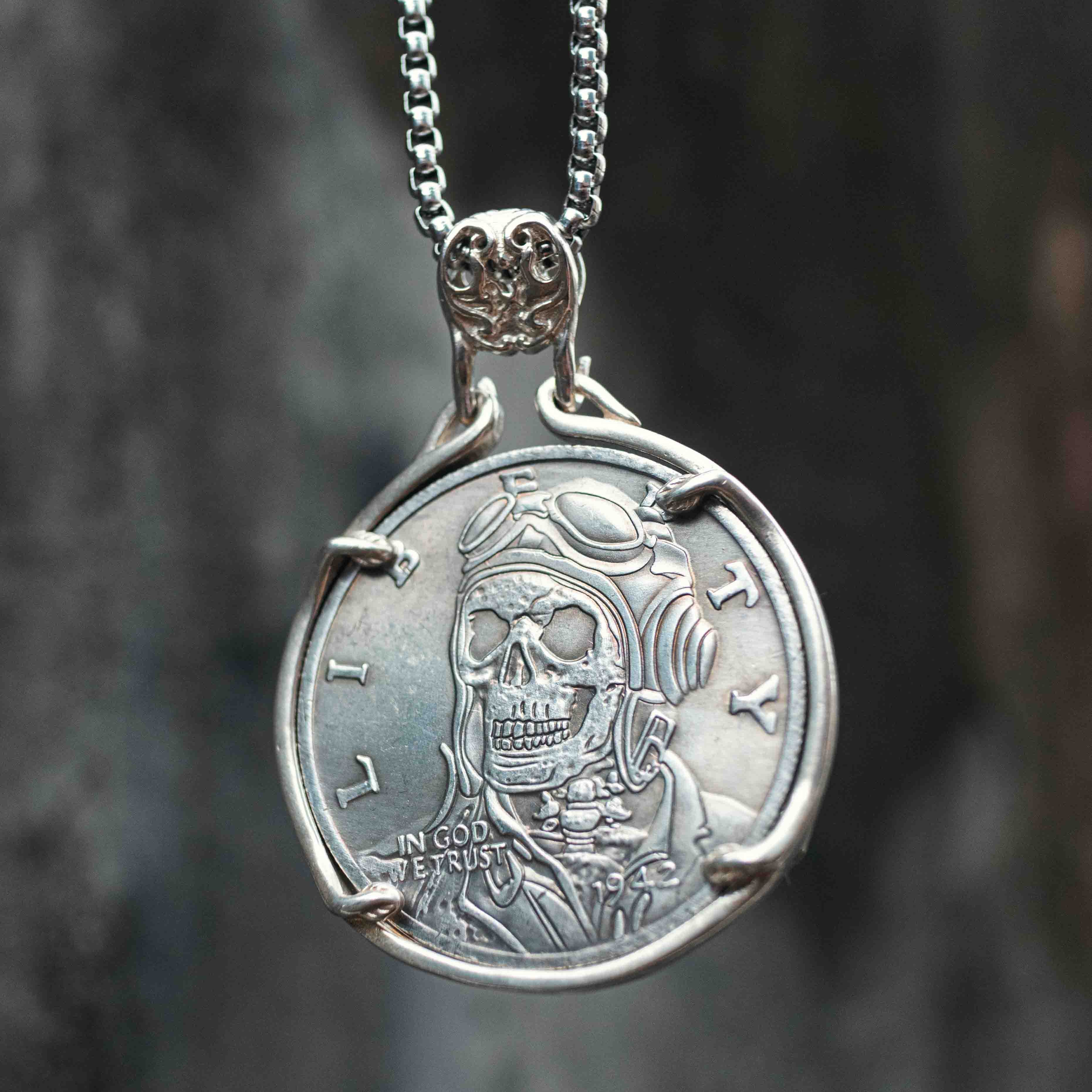 Coin pendant engraved with a skull wearing aviator goggles and flight helmet, Liberty inscription, set in a four-prong bezel with skull bail on a box chain