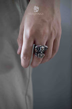Side profile of a skull biker ring on a hand with fingers hanging down, dark blurred background