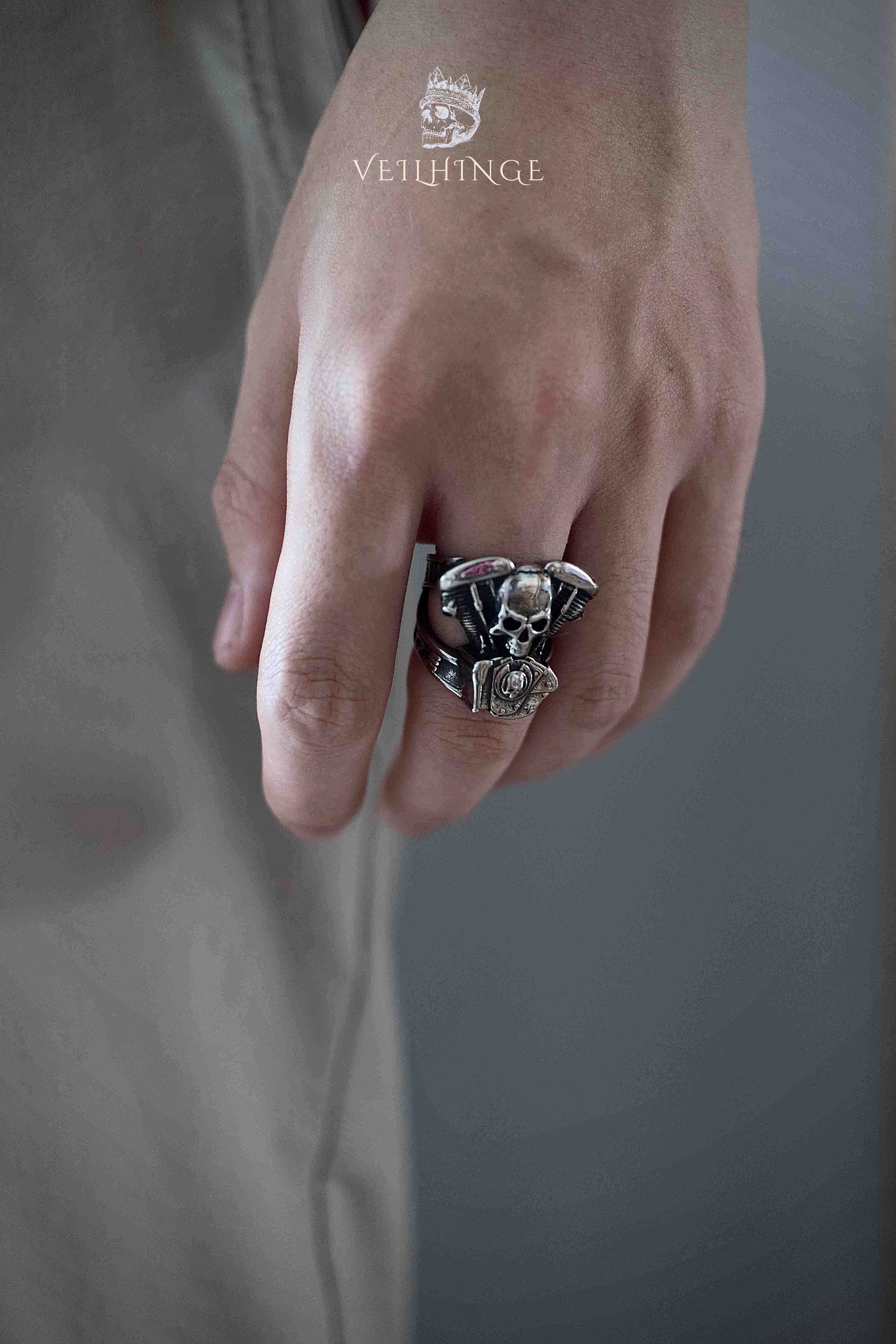 Side profile of a skull biker ring on a hand with fingers hanging down, dark blurred background