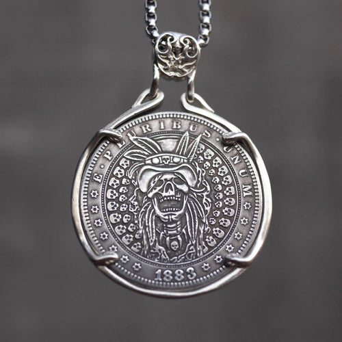 Coin pendant engraved with a skull wearing a Native American war bonnet headdress, surrounded by a border of small skulls, dated 1883, set in a four-prong bezel on a chain