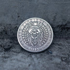 Close-up of a coin engraved with a skull in a feathered war bonnet, ring of small skulls as border decoration, E Pluribus Unum outer edge, dated 1883, on dark stone