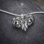 skull heart pendant necklace with twin skull motifs on oxidized dark metal — front view on denim