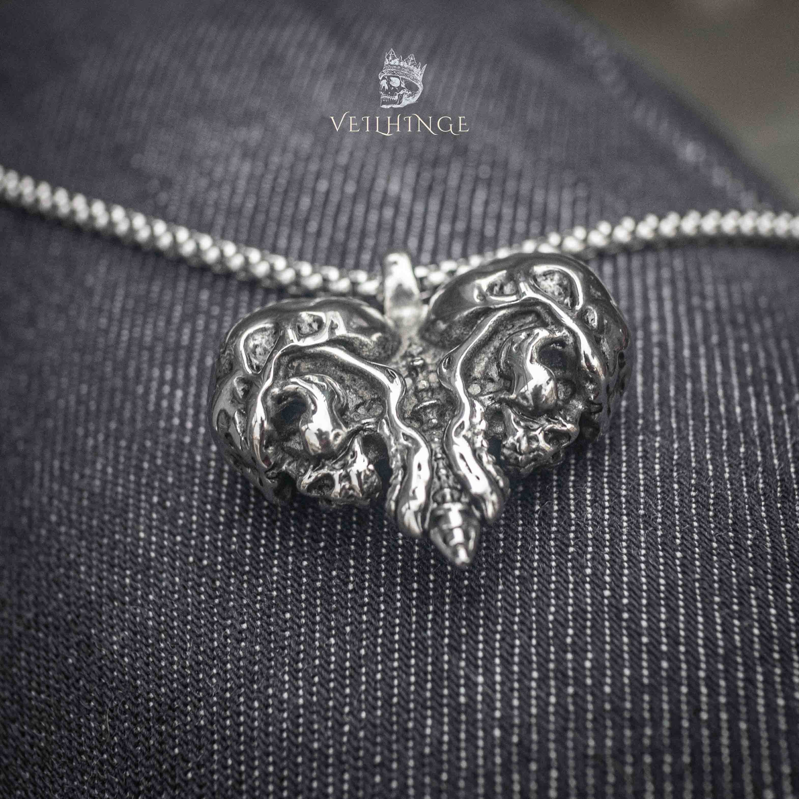 skull heart pendant necklace with twin skull motifs on oxidized dark metal — front view on denim