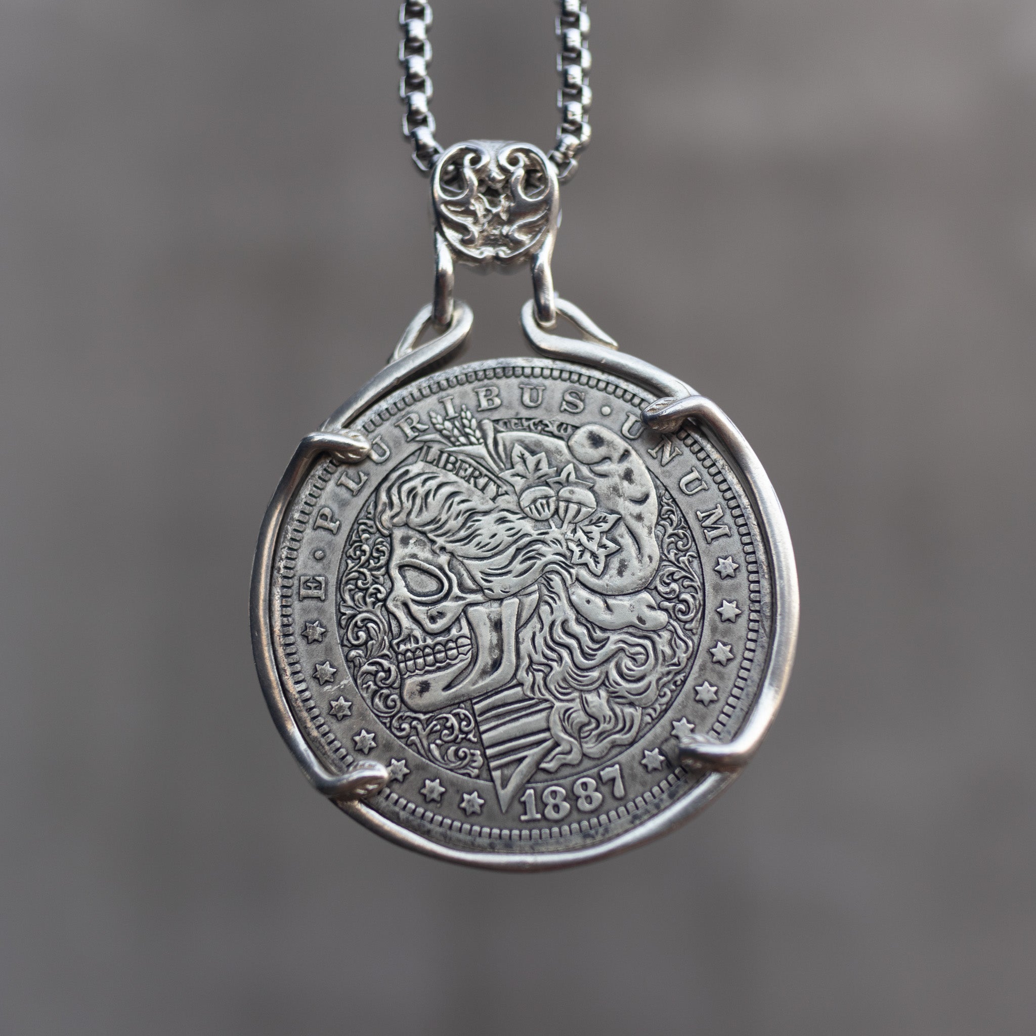 Coin pendant engraved with a skull-faced Lady Liberty with flowing curly hair and wheat crown above a striped shield, dated 1887, in a four-prong bezel on a chain Main image