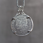 Coin pendant engraved with a skull-faced Lady Liberty with flowing curly hair and wheat crown above a striped shield, dated 1887, in a four-prong bezel on a chain