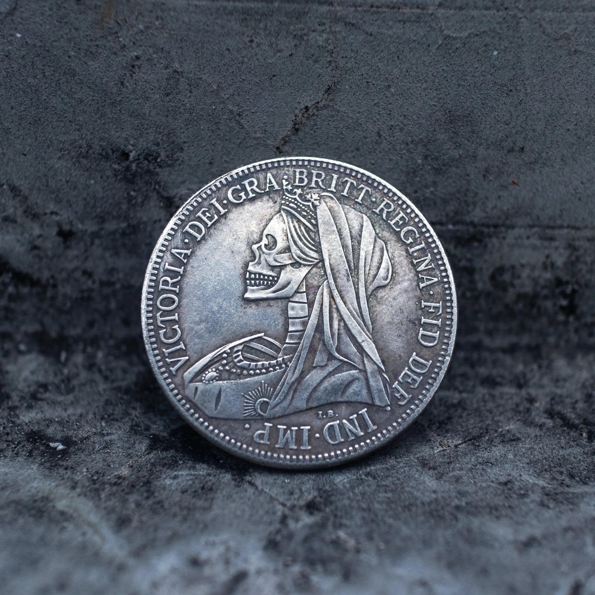Close-up of a coin engraved with a skull in Queen Victoria's mourning veil, Victoria Dei Gra Britt Regina Fid Def Ind Imp inscription around the border, on dark stone