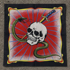 Black bandana laid flat showing a white skull pierced by a dagger with a green snake coiling around it, set against a red sunburst background with gold corner ornaments


