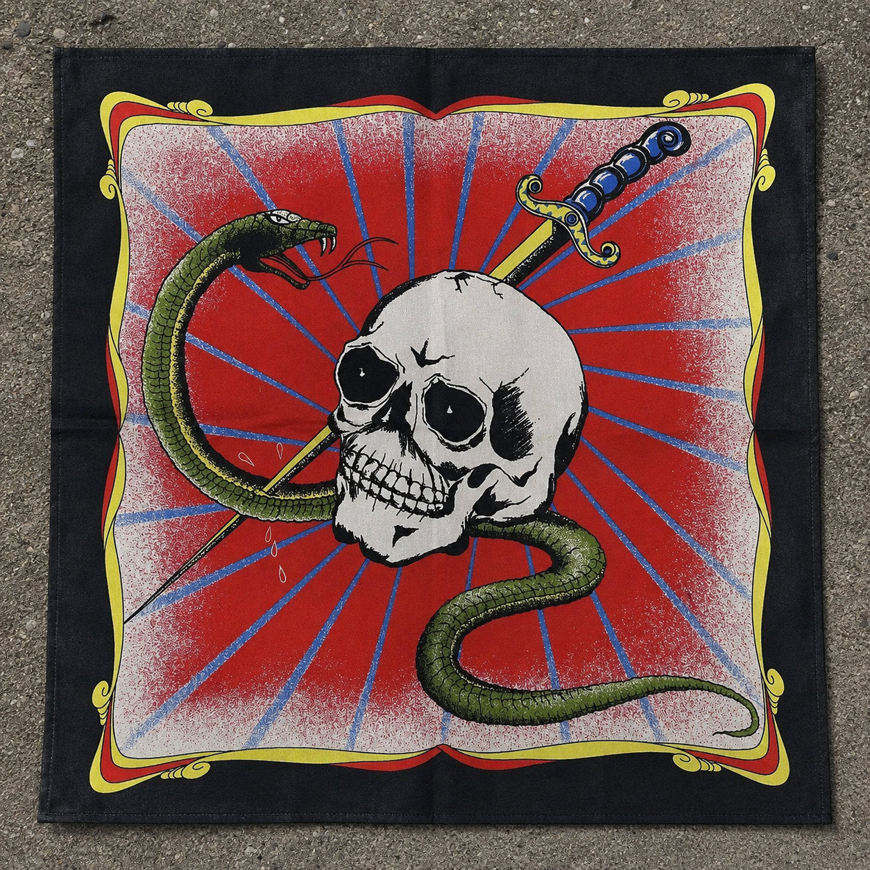 Black bandana laid flat showing a white skull pierced by a dagger with a green snake coiling around it, set against a red sunburst background with gold corner ornaments

