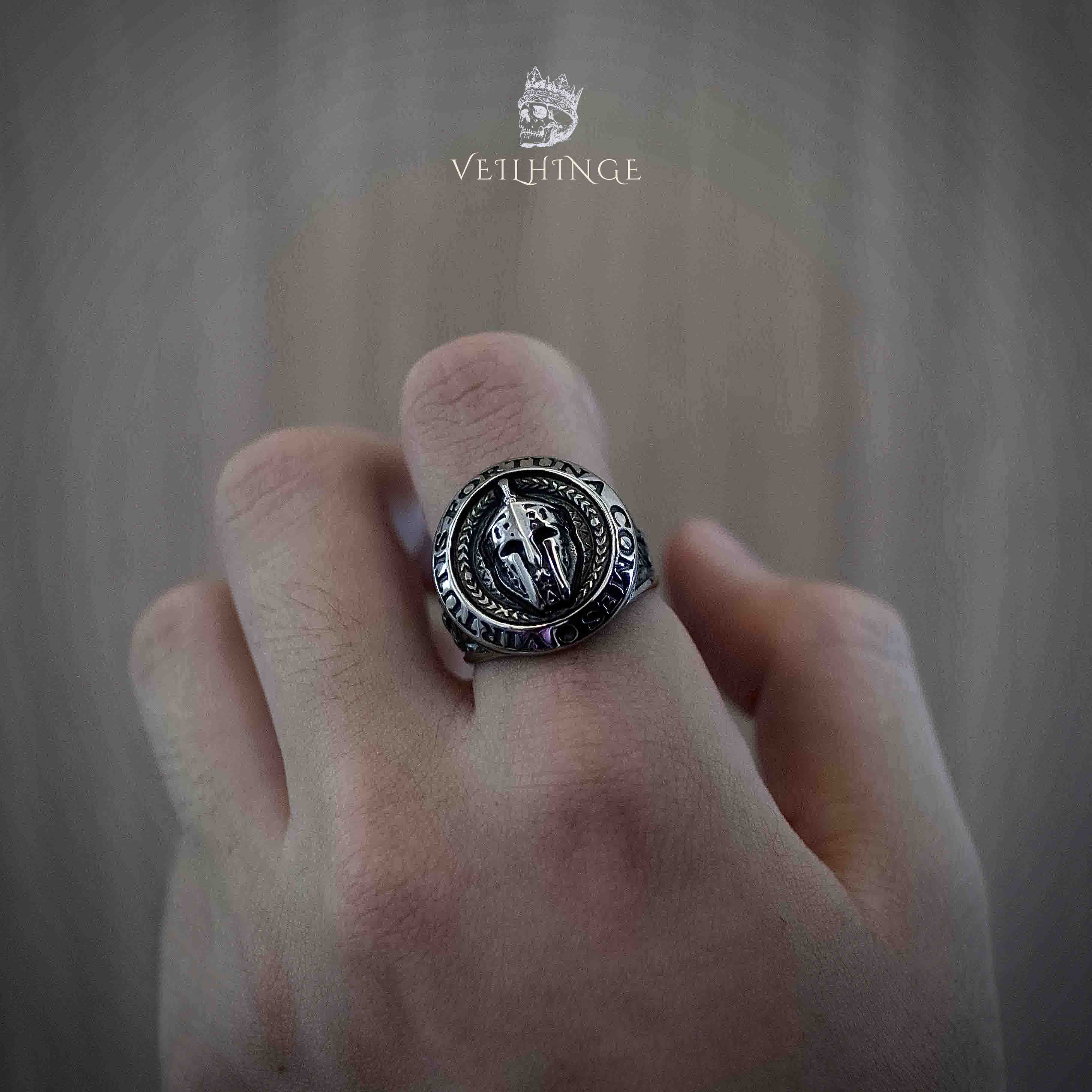 Spartan helmet signet ring with circular inscription worn on a clenched fist, oxidized silver championship-style ring with crossed spears on the face