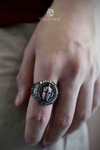 Spartan warrior ring worn on a hand resting flat, showing the ring's large round face and thick oxidized silver band with engraved motto border
