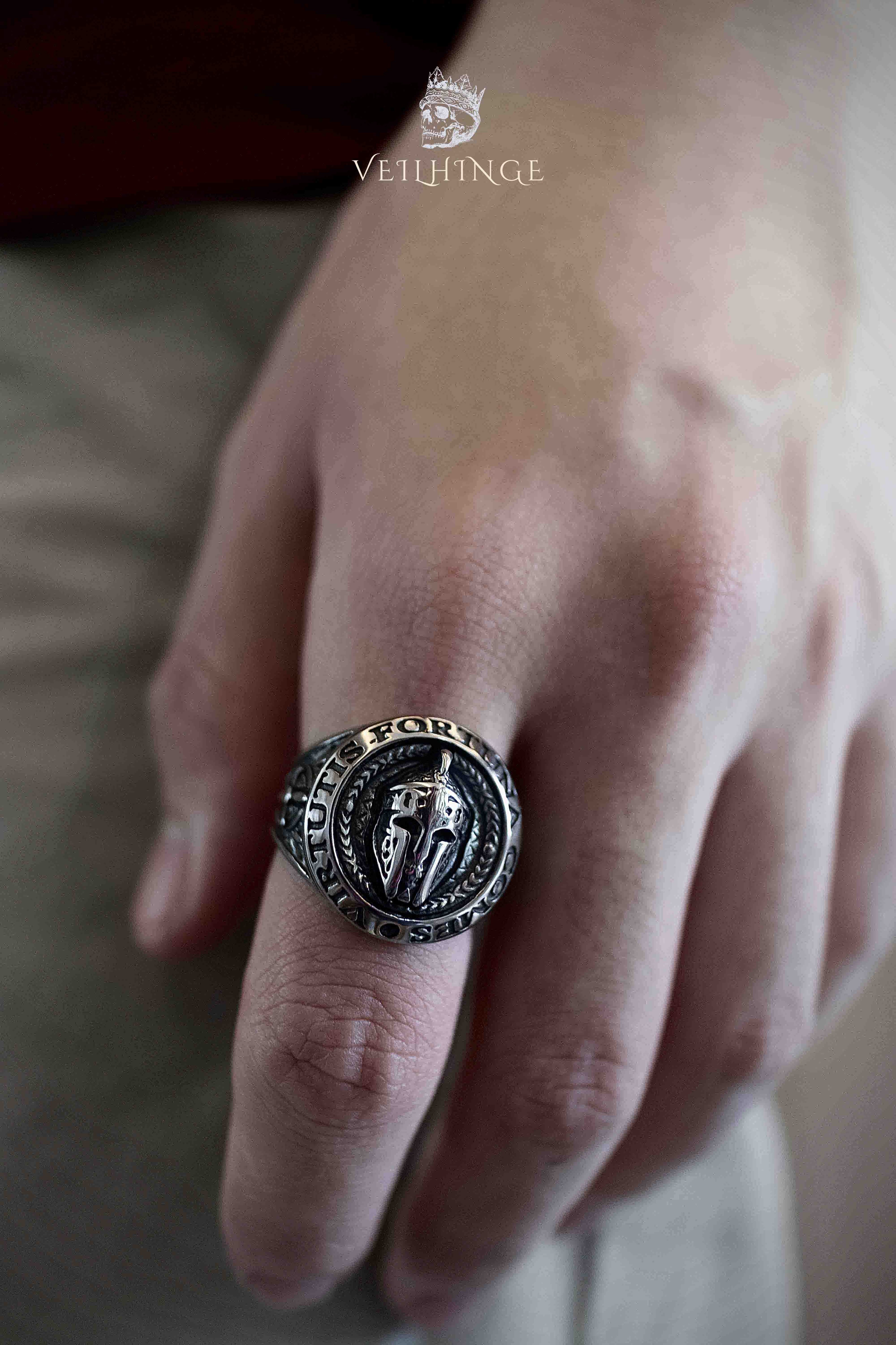 Spartan warrior ring worn on a hand resting flat, showing the ring's large round face and thick oxidized silver band with engraved motto border