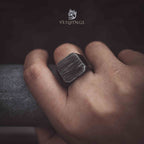 oxidized square ring worn on hand — brushed texture face visible, dark moody lifestyle shot showing scale and fit