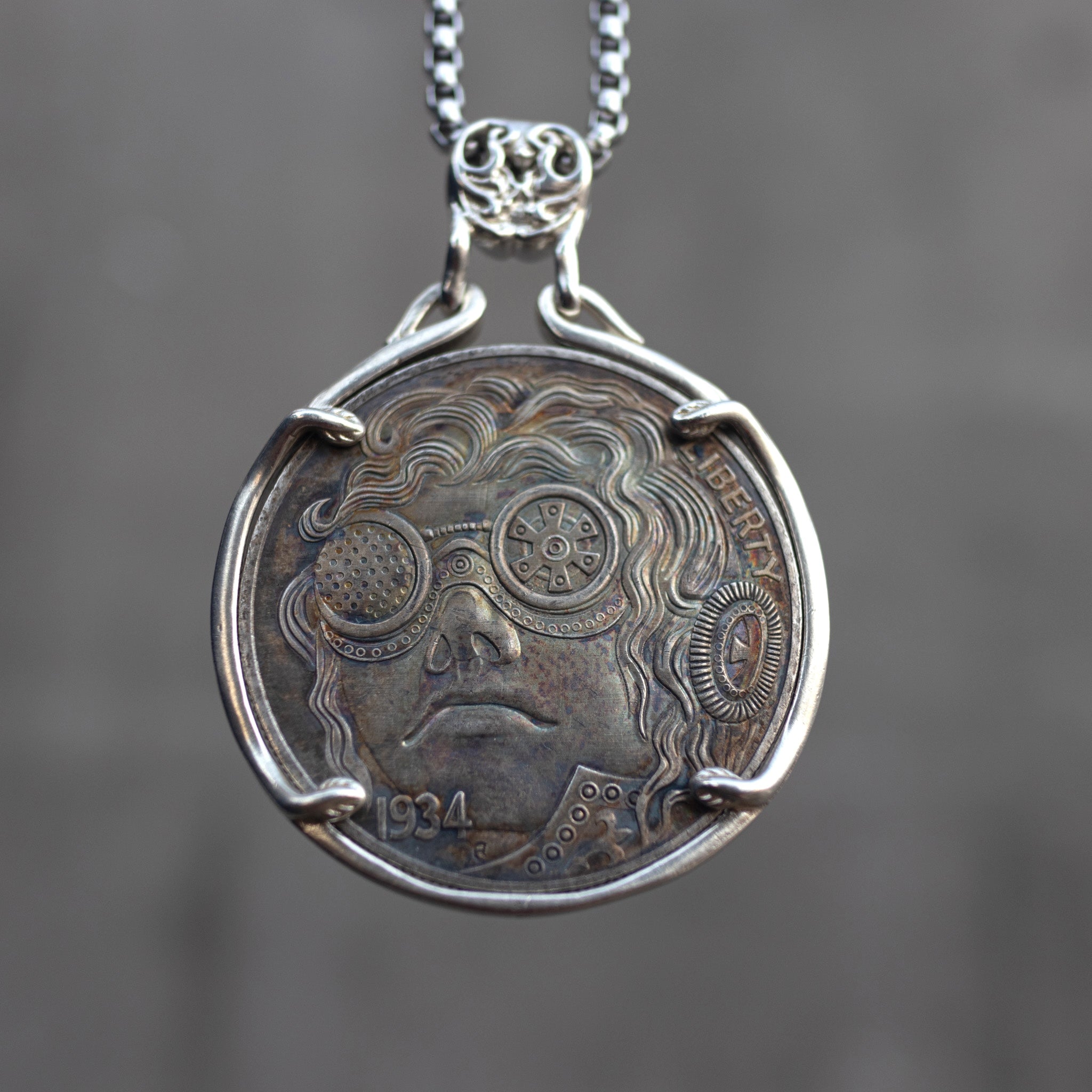 Coin pendant engraved with a steampunk figure wearing gear-detailed round goggles and flowing curly hair, Liberty inscription, dated 1934, set in a four-prong bezel on a chain Main image