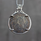 Coin pendant engraved with a steampunk figure wearing gear-detailed round goggles and flowing curly hair, Liberty inscription, dated 1934, set in a four-prong bezel on a chain