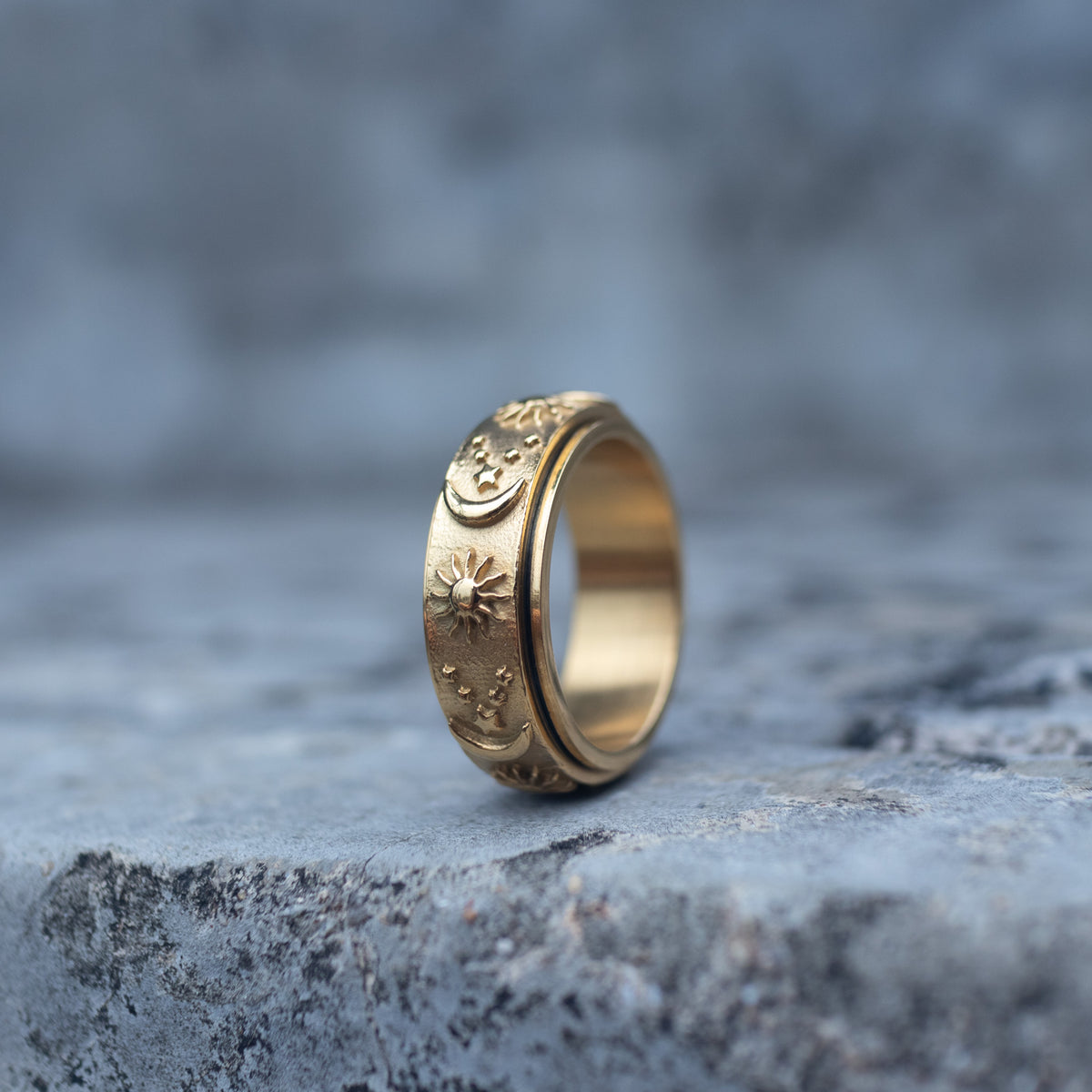Side view of a gold-tone celestial spinner ring with sun, moon and stars