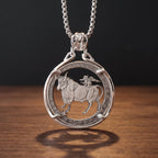 taurus zodiac coin pendant necklace — charging bull with winged cupid figure on back, floral rose border ring, four-prong open frame, ornate skull bail, antique silver tone, warm wood surface