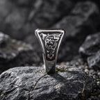 Tiger eye signet ring standing upright in a rock crevice showing the side profile with detailed baroque scroll engraving on the inner band shoulders in dramatic low light