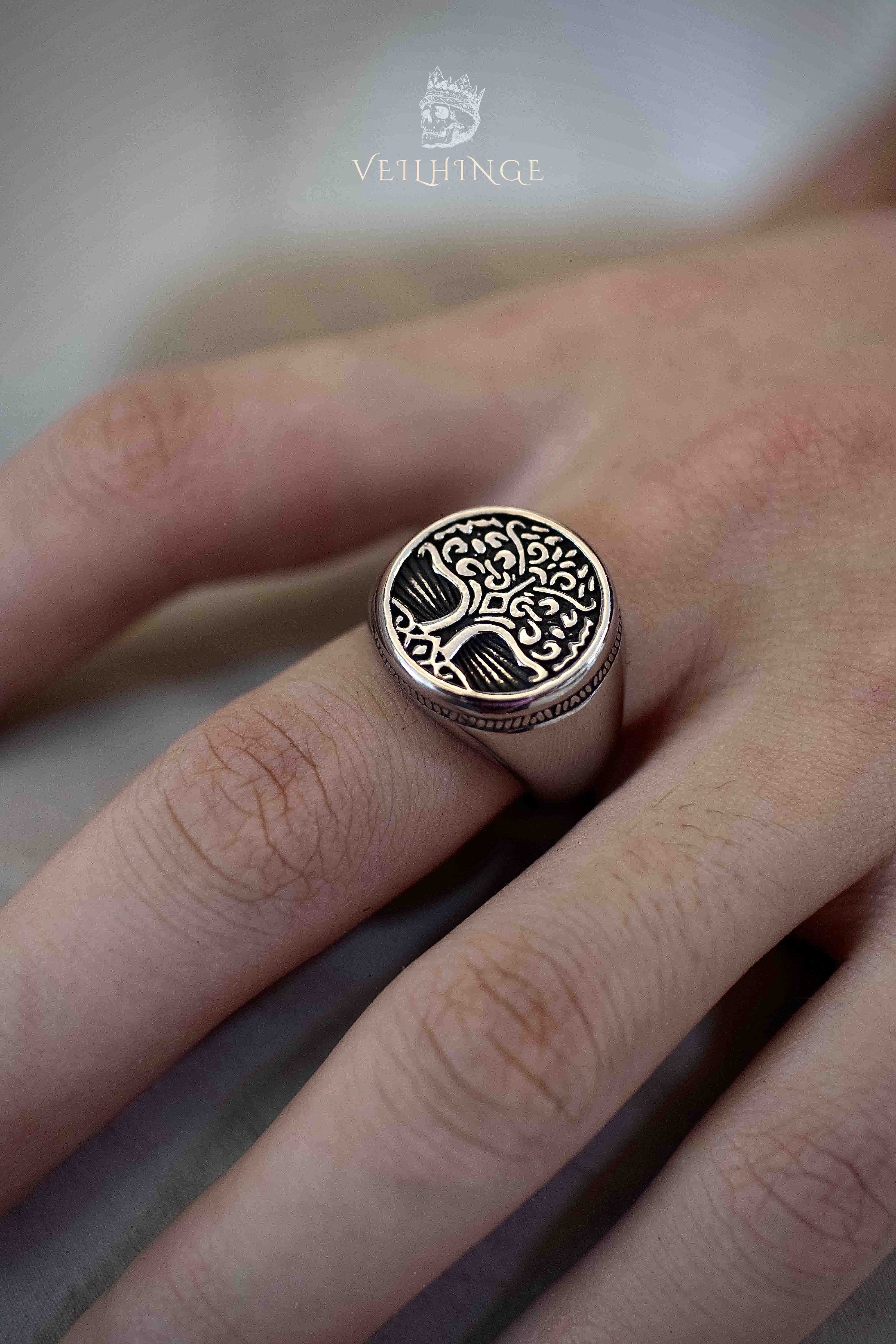 Tree of Life signet ring in oxidized silver worn on a hand, circular face engraved with branches spreading upward and roots below, smooth wide band