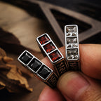 Three square stone signet rings held between fingers showing the white, red, and black gemstone faces side by side, with engraved band detail visible on the sides in low light