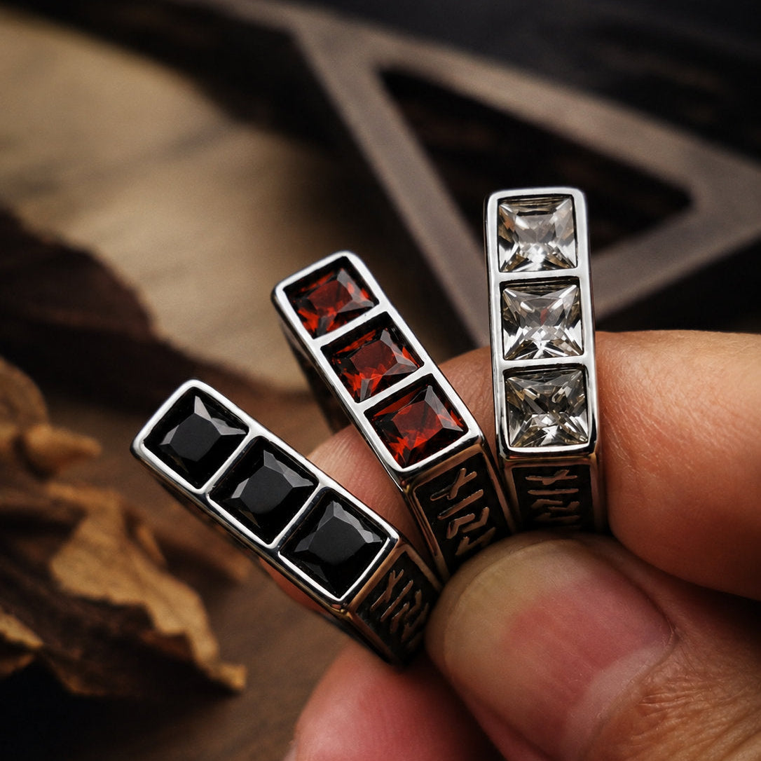 Three square stone signet rings held between fingers showing the white, red, and black gemstone faces side by side, with engraved band detail visible on the sides in low light
