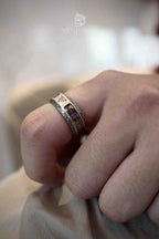 Close-up of a Triquetra rune ring on a bent finger, gold-toned runic symbols embedded in clear resin between Celtic knotwork edges, antique silver finish