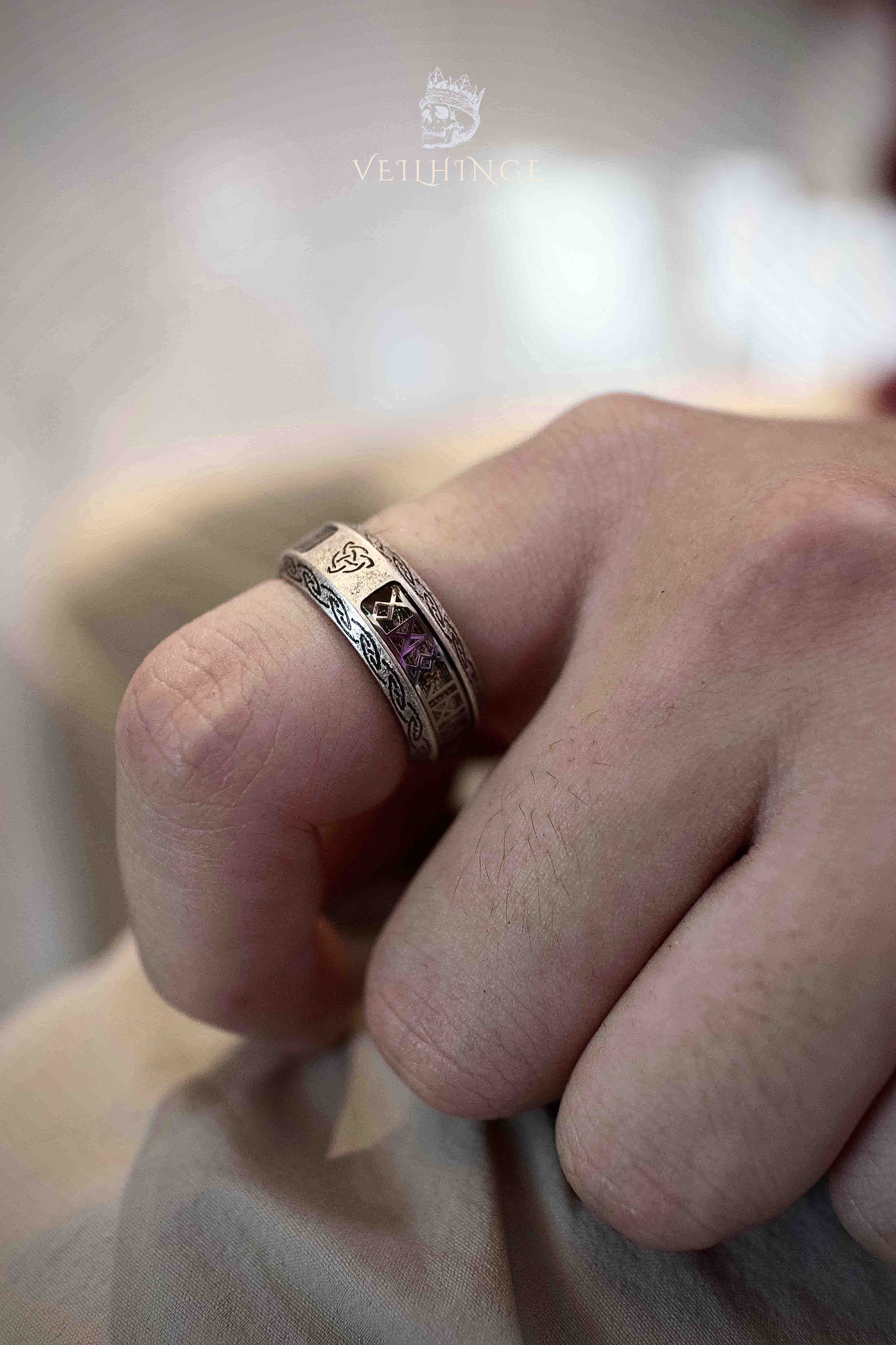 Close-up of a Triquetra rune ring on a bent finger, gold-toned runic symbols embedded in clear resin between Celtic knotwork edges, antique silver finish