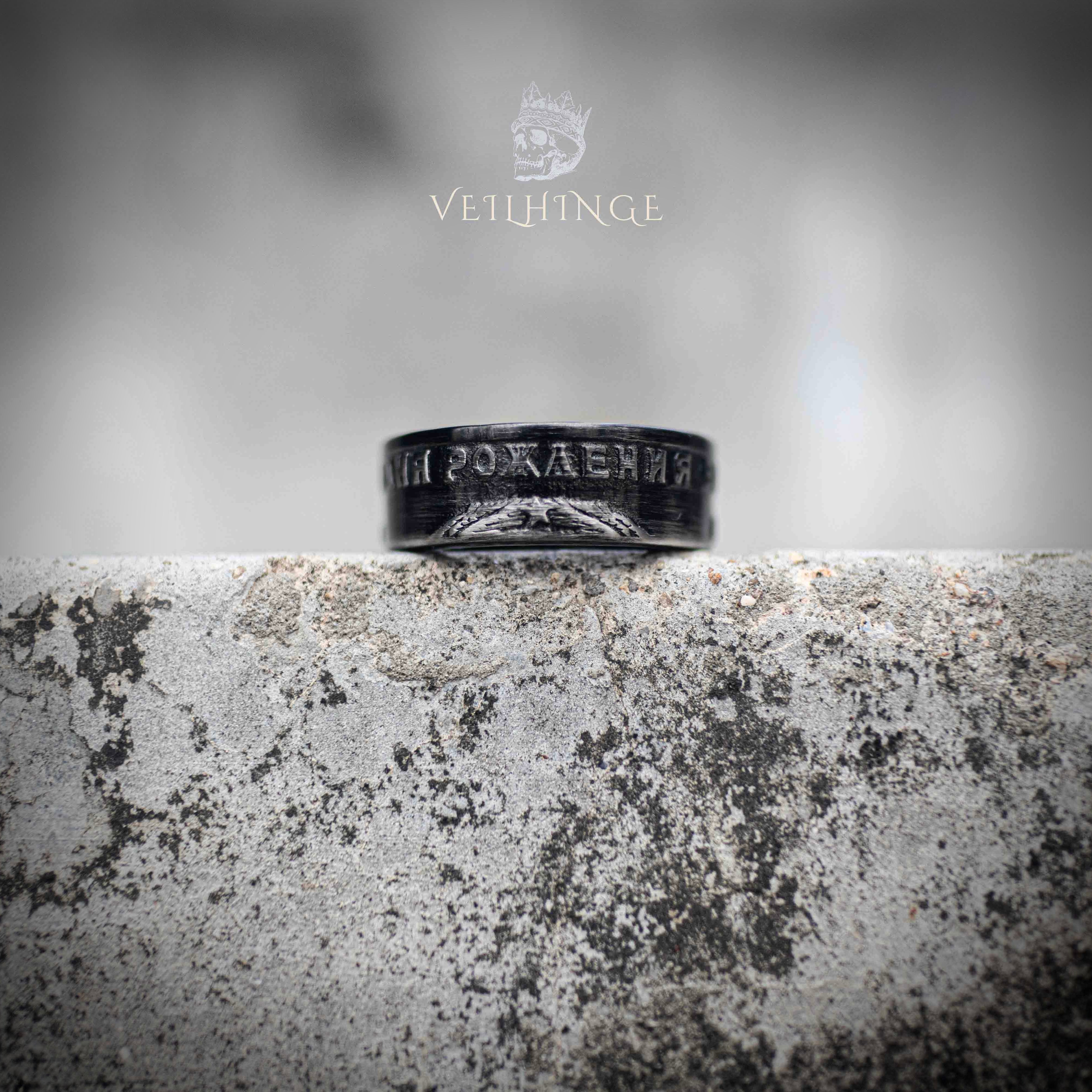 Angled view of black oxidized Soviet coin ring showing partial Cyrillic anniversary text — worn-in dark finish, historical relic aesthetic on weathered stone Main image