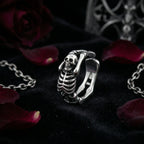 Close-up of Vamp Romantic adjustable skeleton ring with detailed skull and spine design, surrounded by black velvet and red rose petals – tarnish-resistant gothic jewelry